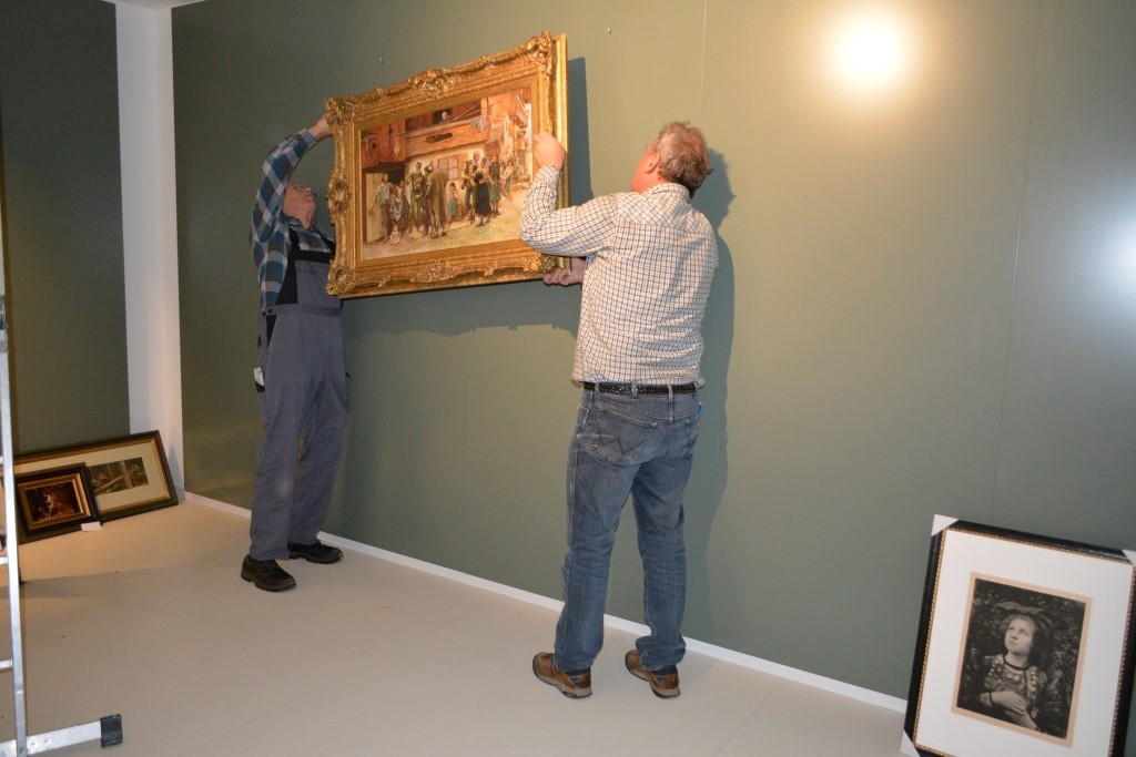 Zwei Männer hängen ein Gemälde auf.