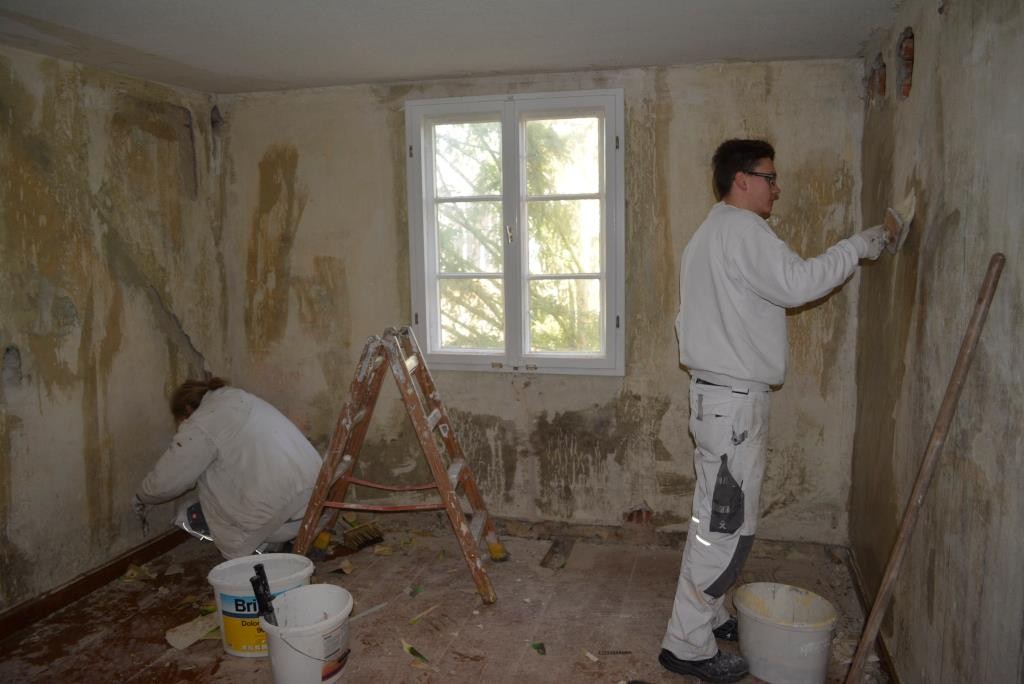 Zwei Maler verputzen und streichen Wände in einem kleinen Raum.