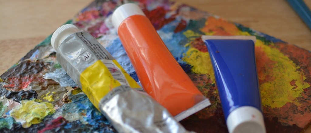 Drei Tuben Acrylfarbe liegen auf einer Malerpalette.